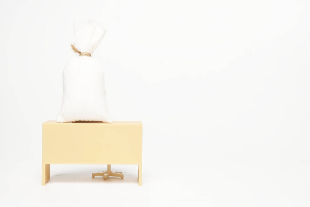 Obrázek miniaturního stolu s peněžním sáčkem na bílém pozadí copyspace. Koncepce mezd a kompenzací - Fotografie, Obrázek