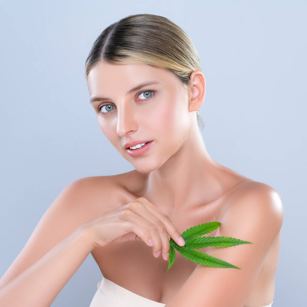 Alluring beautiful woman model portrait holding green leaf as concept for cannabis skincare cosmetic product for skin freshness treatment in isolated background. - 写真・画像