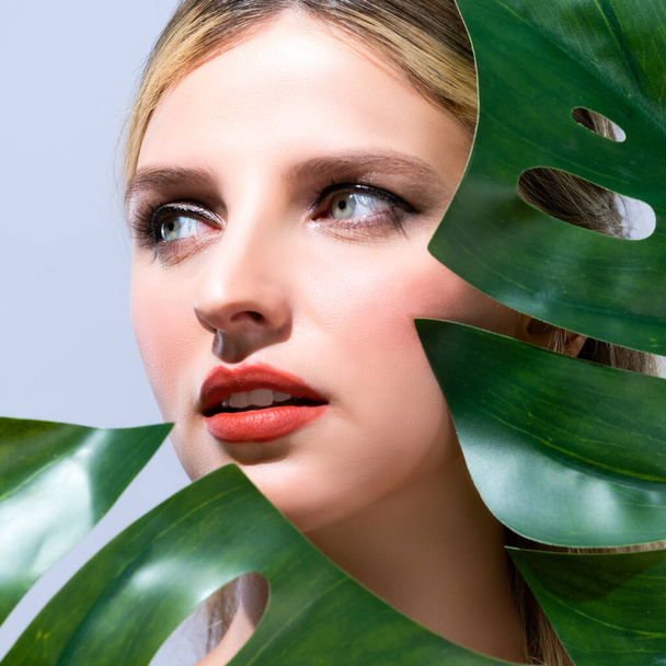 Closeup woman with perfect clean skin and alluring flawless natural soft facial makeup holding green leave monstera. Natural skincare treatment beauty or spa concept in isolated background. - Foto, afbeelding
