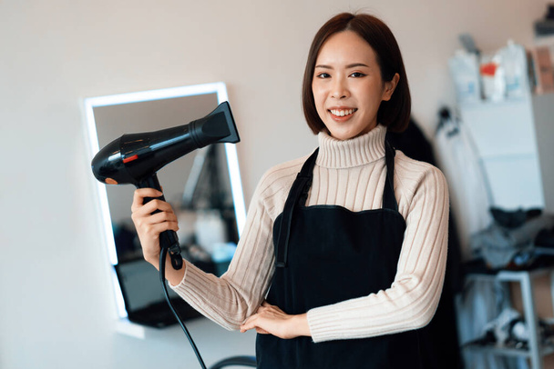 Portrait of a young asian female hairdresser holding qualified haircut tools in her salon for a womans haircut. Photo job concept for small business owner and haircare. - Photo, Image
