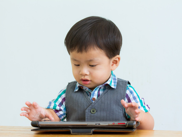 Retrato de un niño sentado en la mesa en un juego en una pestaña digital
 - Foto, imagen