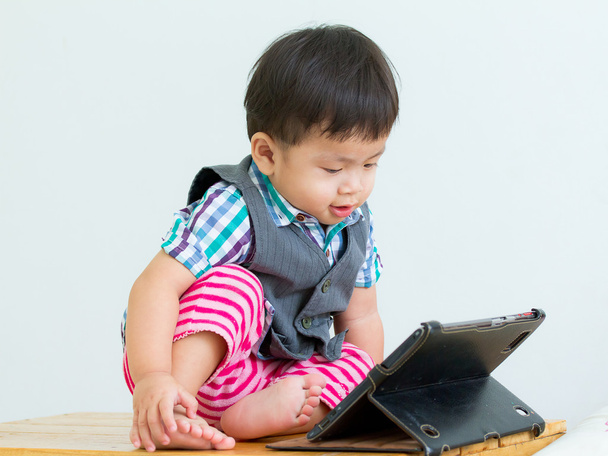 Retrato de uma criança sentada na mesa em um jogo em um tablet digital
 - Foto, Imagem