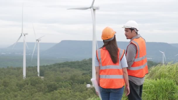 Ingénieurs et ingénieures travaillant dans un parc éolien au sommet d'une colline ou d'une montagne en milieu rural. Idéal progressif pour la production future d'énergie renouvelable et durable. - Séquence, vidéo