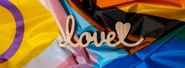 Banner Wooden word love with heart romance on Rainbow LGBTQIA flag made from silk material. Valentines Day greeting card. Symbol of LGBTQ pride month. Equal rights. Peace and freedom. Support LGBTQIA - Foto, imagen