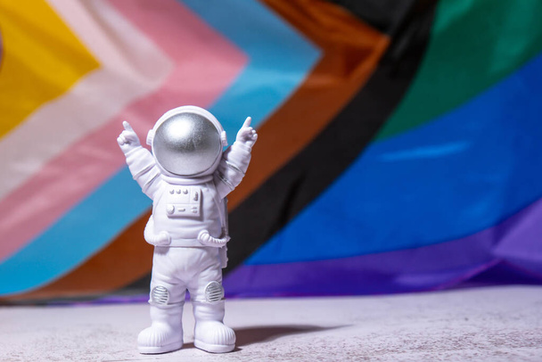 Toy astronaut on Rainbow LGBTQIA flag made from silk material background. Happy pride month. Symbol of LGBTQ pride month. Equal rights. Peace and freedom. Support LGBTQIA community. Diversity equality - 写真・画像
