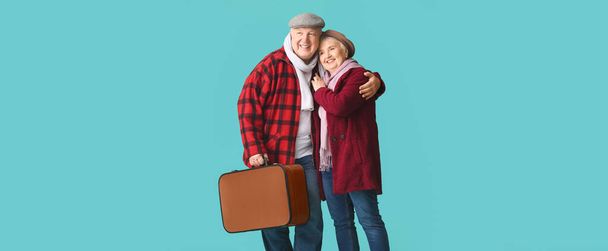Glückliches Seniorenpaar mit gepacktem Koffer auf blauem Hintergrund - Foto, Bild
