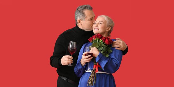Pareja madura con vino y flores sobre fondo rojo - Foto, Imagen