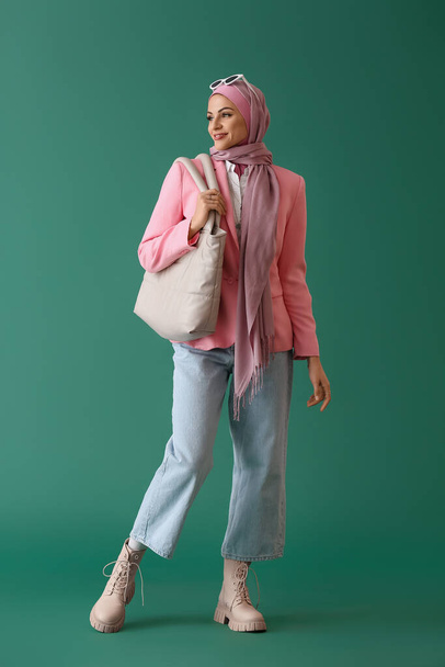 Stylish Muslim woman in pink hijab with bag on green background - 写真・画像