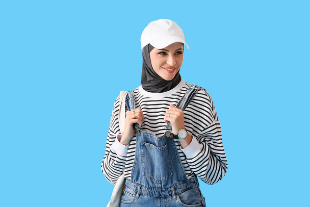 Femme musulmane élégante en casquette avec sac sur fond bleu - Photo, image