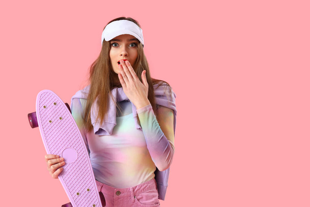 Shocked young woman with skateboard on pink background - Foto, afbeelding