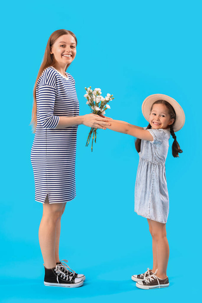 Χαριτωμένο κοριτσάκι χαιρετάει τη μητέρα της με λουλούδια σε μπλε φόντο - Φωτογραφία, εικόνα