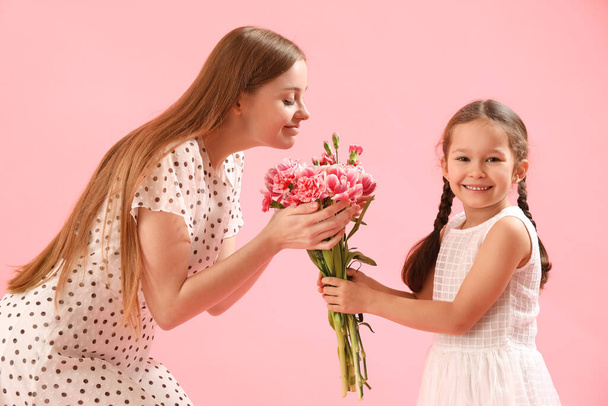Cute little girl greeting her mother with flowers on pink background - 写真・画像