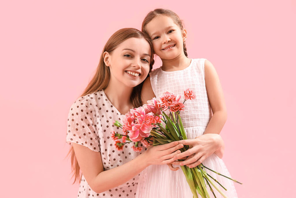 Cute little girl and her mother with flowers hugging on pink background - Foto, afbeelding