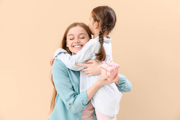 Cute little girl hugging her mother with gift on beige background - Valokuva, kuva