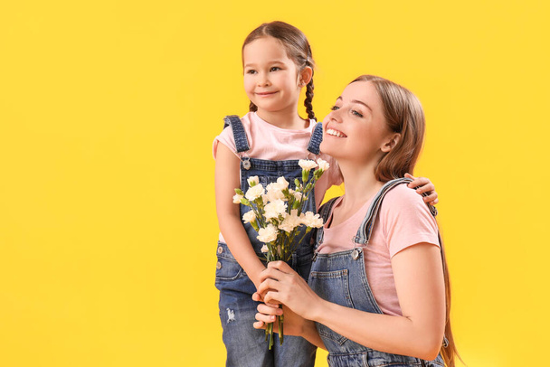 Petite fille mignonne et sa mère avec des fleurs sur fond jaune - Photo, image