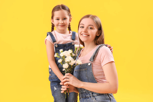 Cute little girl and her mother with flowers on yellow background - Photo, image
