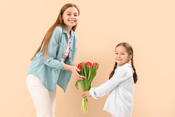 Cute little girl greeting her mother with tulips on beige background - Foto, immagini