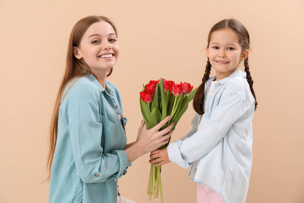 Cute little girl greeting her mother with tulips on beige background - 写真・画像