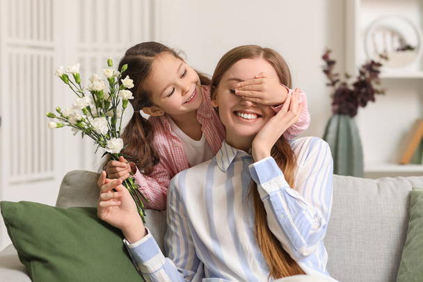 Little girl with flowers closing her mother's eyes at home - Foto, Bild