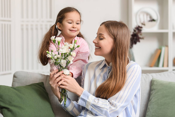 schattig klein meisje groeten haar moeder met bloemen thuis op vakantie - Foto, afbeelding