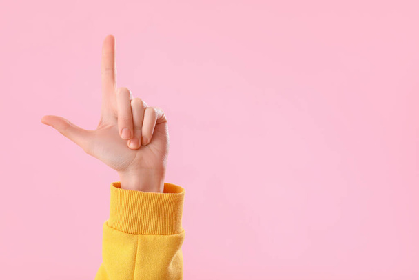 Young woman showing loser gesture on pink background - Foto, afbeelding