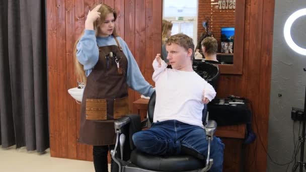 a young man with disabilities discusses his hairstyle with his master in a barber shop - Video