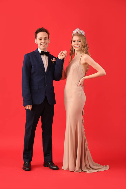 Beautiful couple dressed for prom holding hands on red background - Zdjęcie, obraz