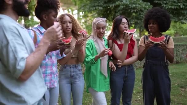 amigos multirraciales comiendo sandía en el parque - Imágenes, Vídeo