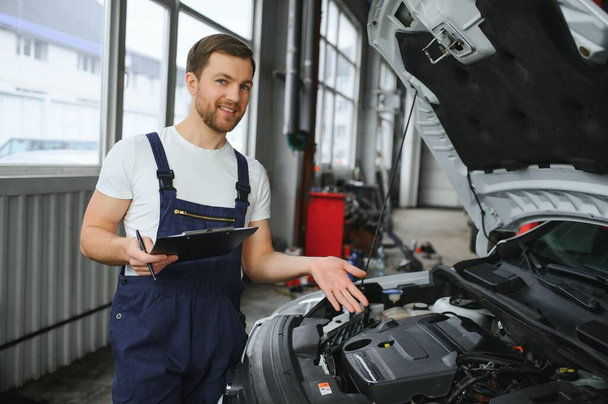 car service, repair, maintenance and people concept - happy smiling auto mechanic man or smith with clipboard at workshop. - Фото, зображення