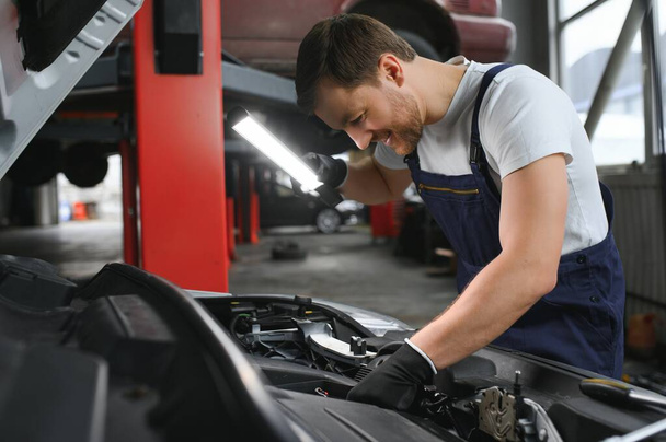 A mechanic is doing car checkup under the hood with flashlight at mechanic's shop - Фото, зображення