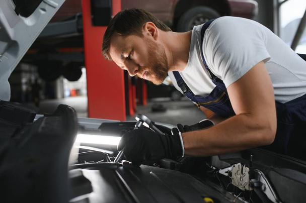 Auto mechanic working on car engine in mechanics garage. Repair service - Фото, изображение