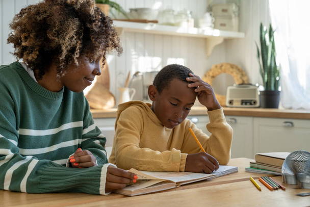 Gemeinsam Hausaufgabenbetreuung. Fürsorgliche afroamerikanische Mutter hilft nachdenklichem Adoptivsohn bei Hausaufgaben für effektive Bildung. Aufmerksam privat schwarz tutor frau geben lektion nachdenklich junge - Foto, Bild