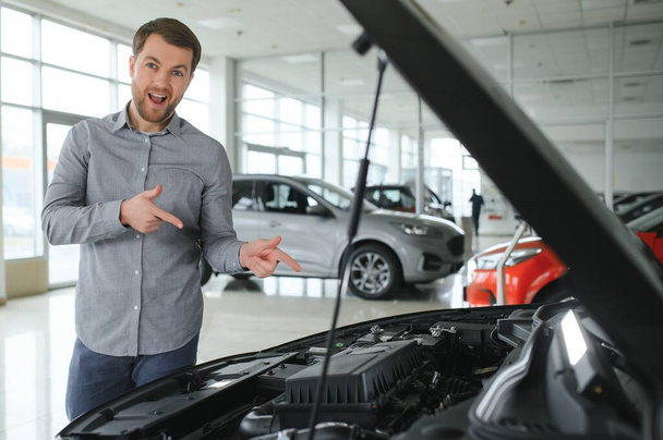 Looks under the hood of automobile. Young man in the car dealership - Foto, afbeelding