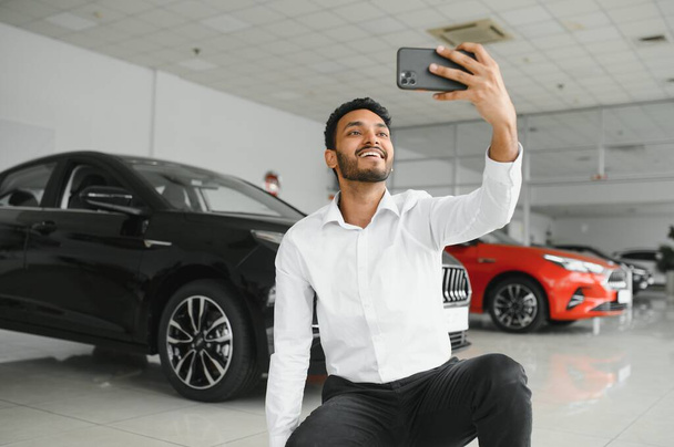 Handsome indian man taking a selfie with car keys to his new automobile at the dealership - Foto, Imagem