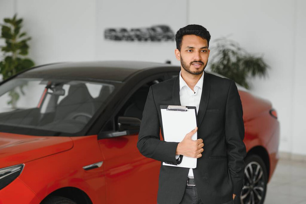 indian cheerful car salesman showing new car at showroom. - Fotó, kép