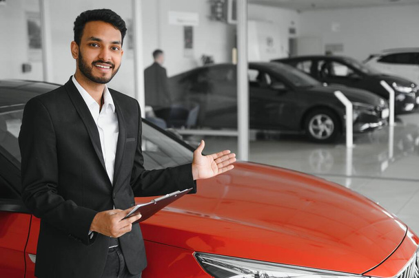 Good looking, cheerful and friendly indian salesman poses in a car salon or showroom - Zdjęcie, obraz