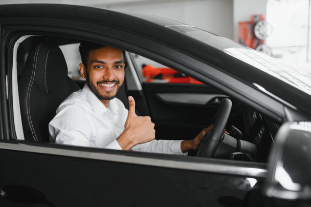 Young man sitting inside new car. Smiling. - Фото, изображение