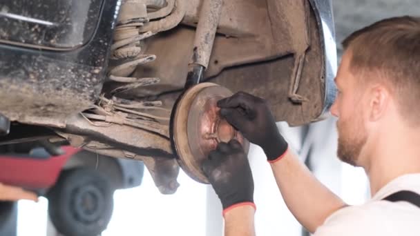 De monteur controleert het chassis op schade of slijtage. Reparatie van het chassis van de auto in het autobedrijf. - Video