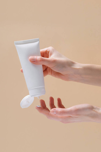 Vertical image of female hands squeezing cream from a blank tube on a finger on a beige isolated background. The concept of beauty and aesthetics. Image for your design - Foto, Imagem