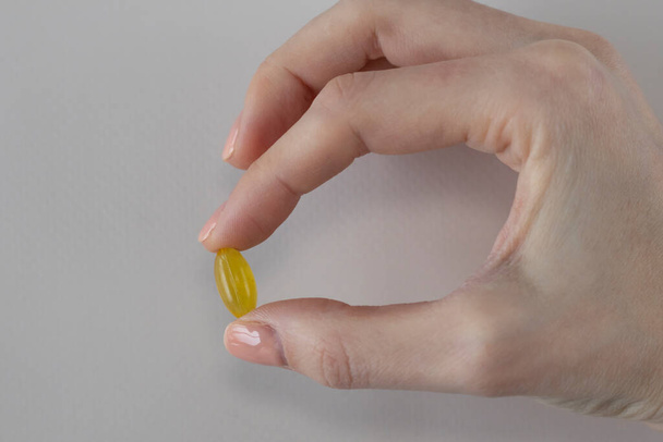 Gele capsule van oregano olie supplement in een vrouwenhand. - Foto, afbeelding
