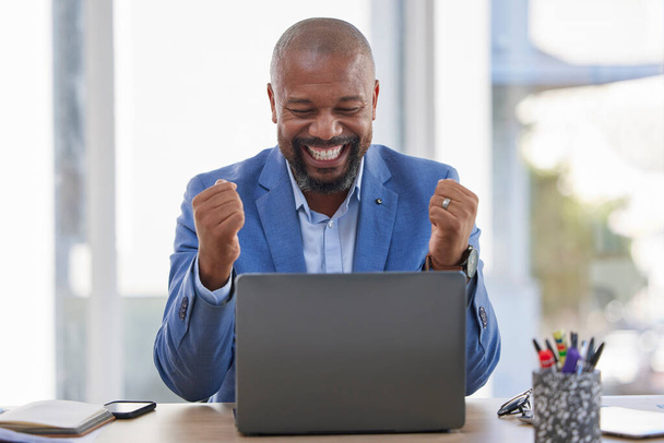 Happy black man, laptop and celebration for winning, sale or good news on discount at the office desk. Excited African American male celebrating on computer for promotion, bonus or achievement. - 写真・画像
