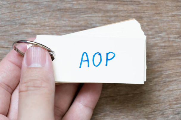 Hand hold flash card with handwriting in word AOP (abbreviation of Annual Operating Plan or Aspect-oriented programming) on wood background - Valokuva, kuva