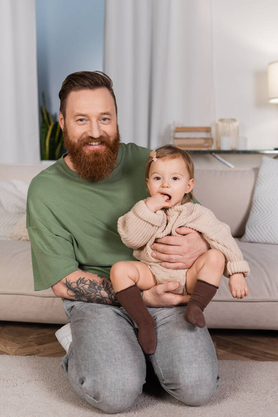 Cheerful tattooed dad holding baby girl at home  - Φωτογραφία, εικόνα