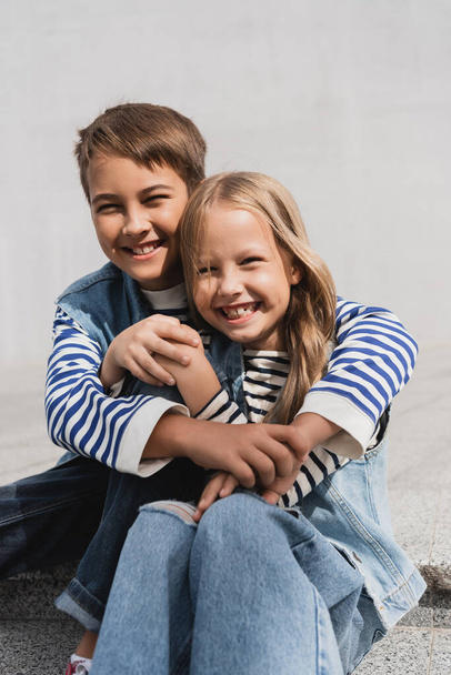 happy preteen boy in hugging well dressed girl while sitting on stairs  - Photo, image