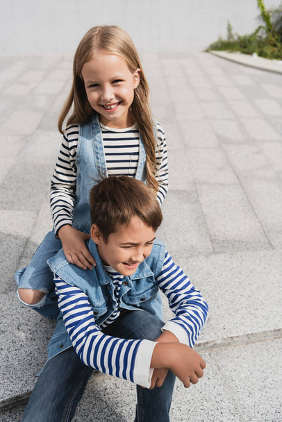 pleased girl in stylish clothes leaning on shoulders of well dressed boy  - Photo, Image
