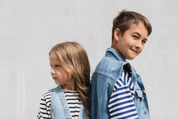 well dressed boy and girl in denim outfits looking at camera while standing outdoors  - Foto, Imagen
