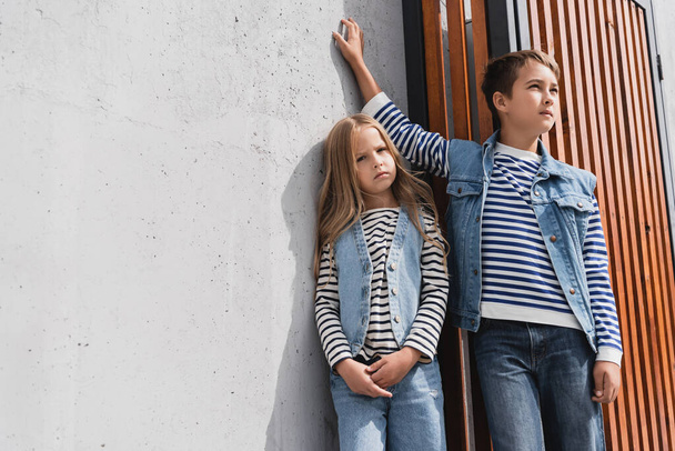 stylish preteen boy in denim vest leaning on wall while standing with girl near mall  - Photo, Image