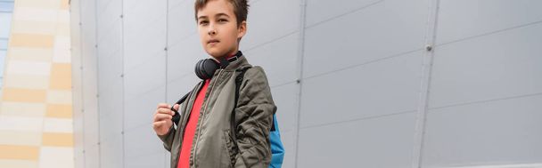 preteen boy in wireless headphones standing with backpack near mall, banner  - Foto, immagini