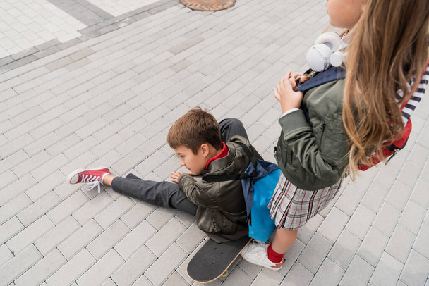 overhead view of preteen boy in stylish bomber jacket sitting on penny board near girl in wireless headphones  - Φωτογραφία, εικόνα
