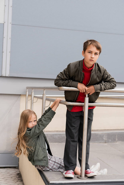 well dressed preteen kids in bomber jackets posing near metallic handrails near mall  - Foto, immagini